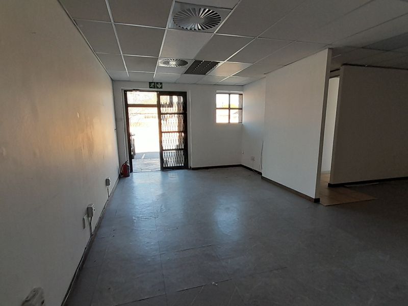An empty office space featuring a suspended ceiling, recessed lighting, and a secure entrance gate, ready for customization.