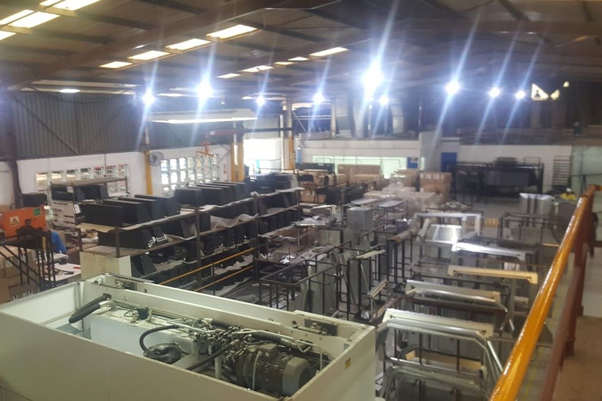 Elevated view of an industrial warehouse space featuring high-bay lighting, steel roof trusses, and a mezzanine level with safety railing.