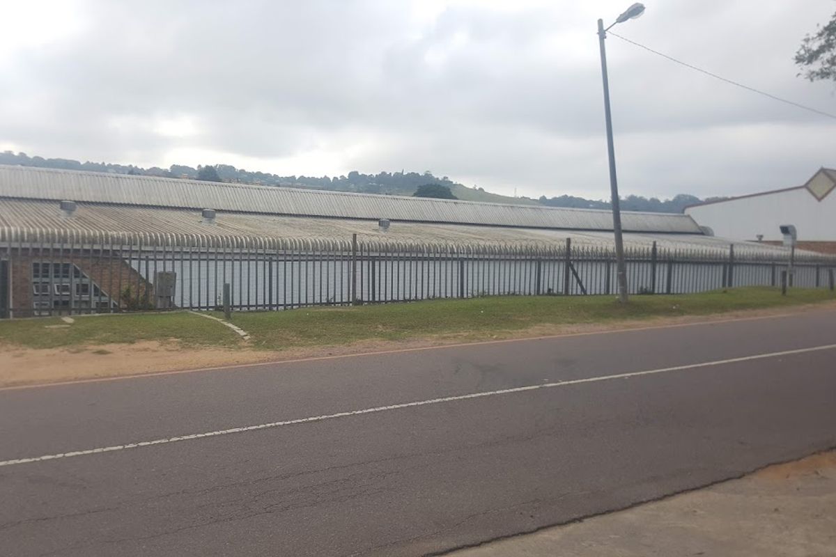 Street view of an industrial property featuring a large corrugated metal roof and perimeter security fencing.