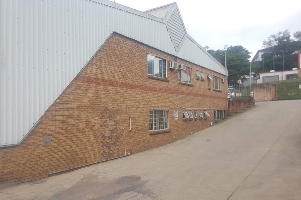 Exterior view of an industrial building featuring a face brick facade, corrugated metal upper cladding, and security-fitted windows along a concrete driveway.