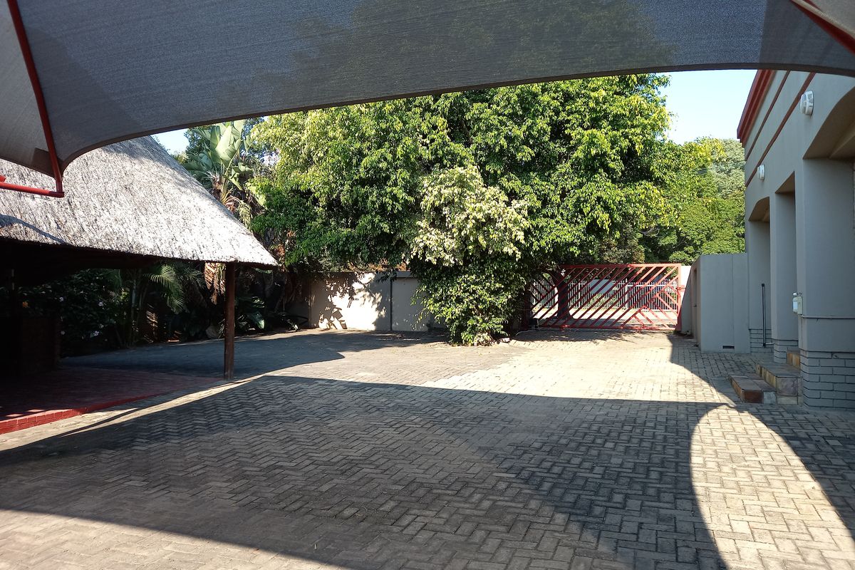 Spacious paved outdoor area featuring a thatch roof lapa, shade sail coverage, and secure gated access, suitable for parking or outdoor utility use.