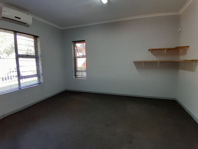 A vacant office space featuring carpeted flooring, wall-mounted shelving, venetian blinds, and a split-system air conditioning unit.