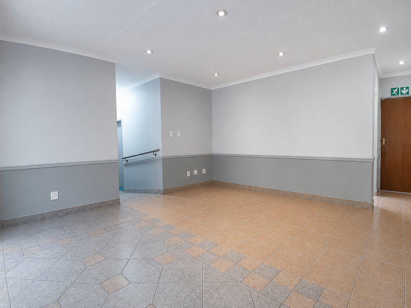 A spacious, empty office area featuring neutral grey walls, a dado rail, tiled flooring, and recessed downlighting, suitable for a professional workspace.
