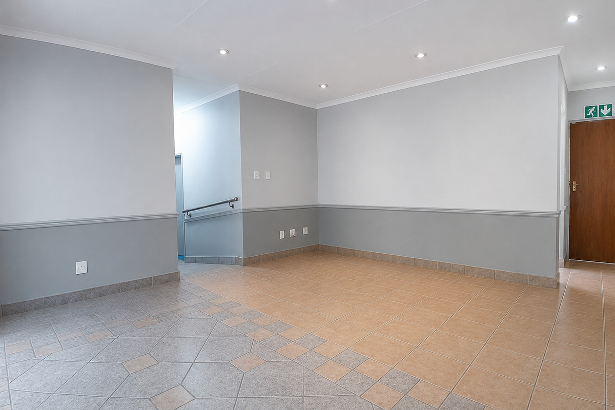 A spacious, empty office area featuring neutral grey walls, a dado rail, tiled flooring, and recessed downlighting, suitable for a professional workspace.