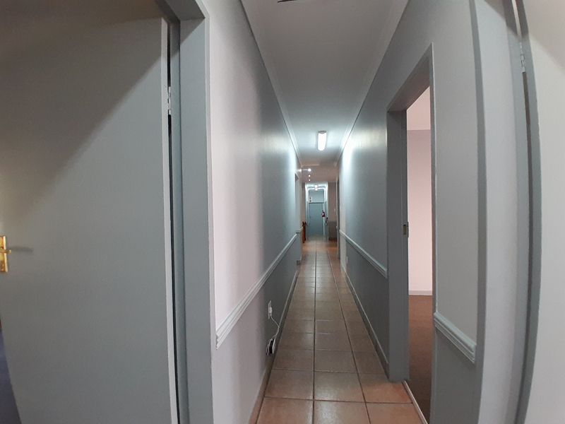 A long, tiled office hallway featuring neutral wall tones, chair rail molding, and multiple access points to adjacent office spaces.