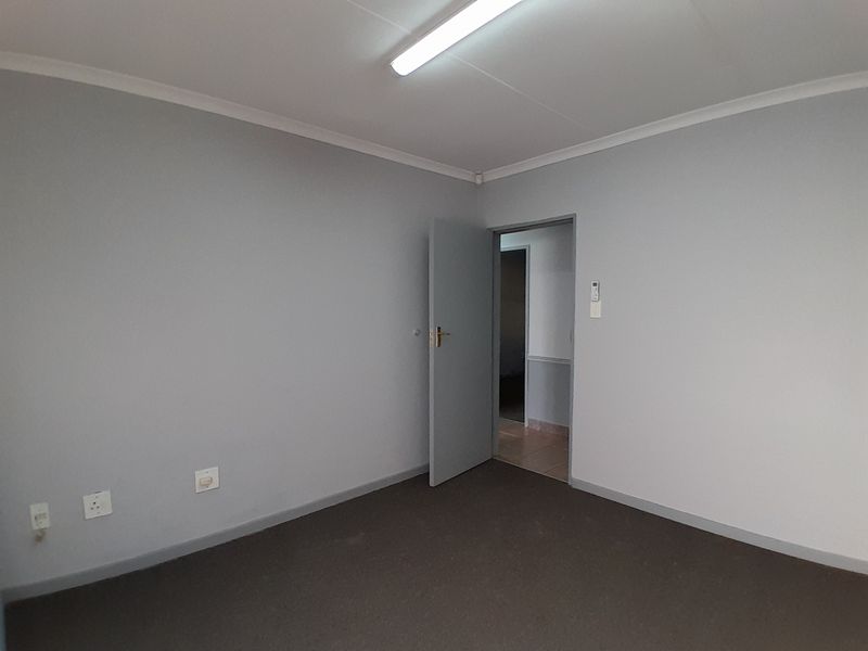A clean, empty office space featuring neutral grey walls, carpeted flooring, and a standard fluorescent light fixture, ready for professional use.