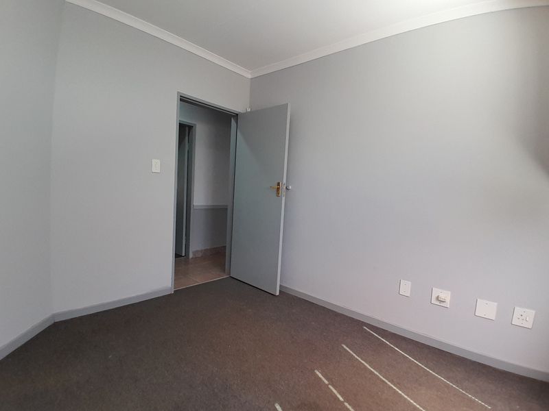 A clean, empty office space featuring neutral grey walls, carpeted flooring, and multiple electrical points, ready for professional use.