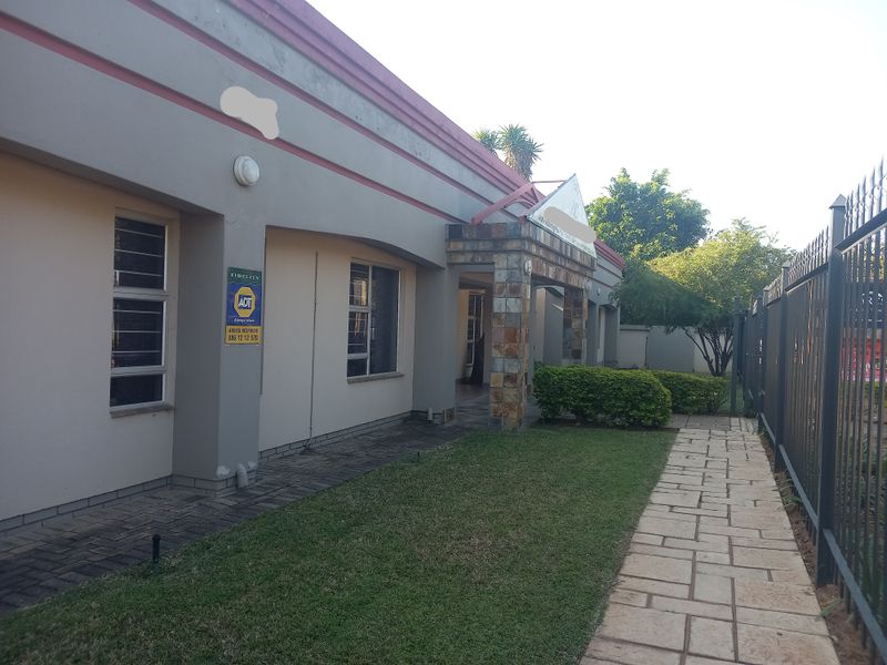 Front exterior view of the office building featuring a stone-clad entrance, paved walkway, and secure perimeter fencing.