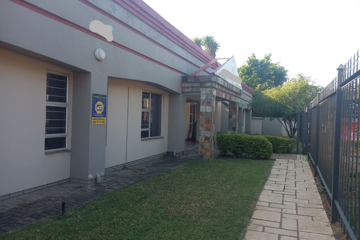 Front exterior view of the office building featuring a stone-clad entrance, paved walkway, and secure perimeter fencing.