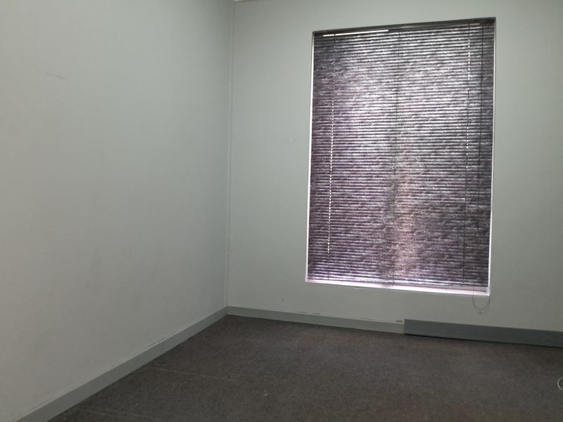 An empty office space featuring grey carpet flooring, neutral walls, and fitted venetian blinds, providing a blank canvas for a professional workspace.