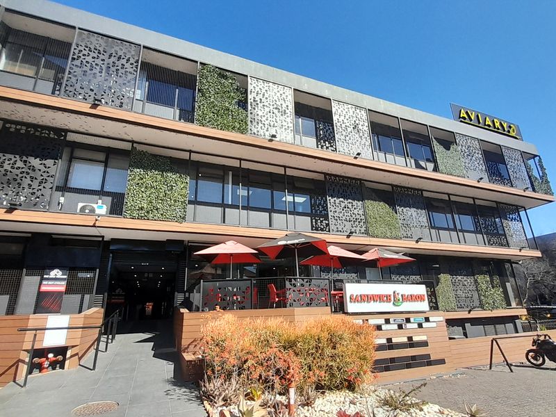 Modern multi-story office building exterior featuring decorative metal screens, vertical garden elements, and a paved ground-level entrance area with commercial signage.