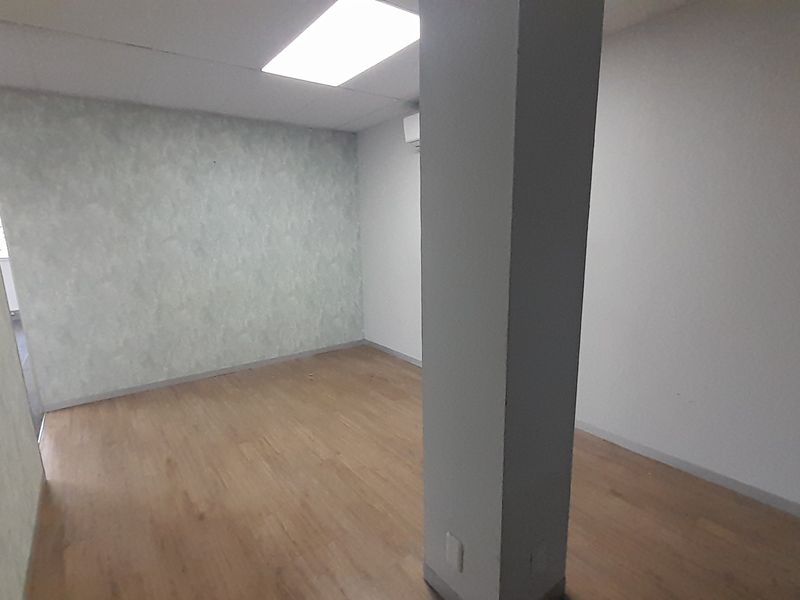 An empty office space featuring laminate flooring, a structural column, recessed ceiling lighting, and a wall-mounted air conditioning unit.