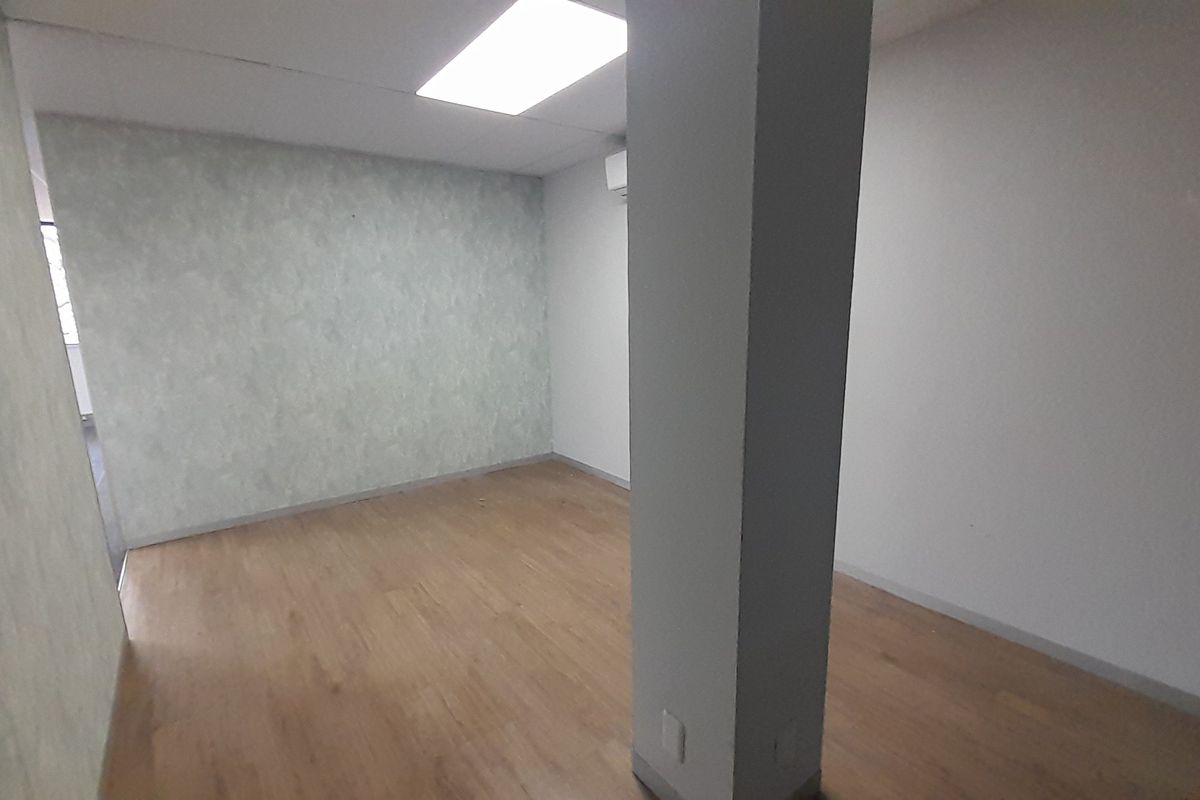 An empty office space featuring laminate flooring, a structural column, recessed ceiling lighting, and a wall-mounted air conditioning unit.