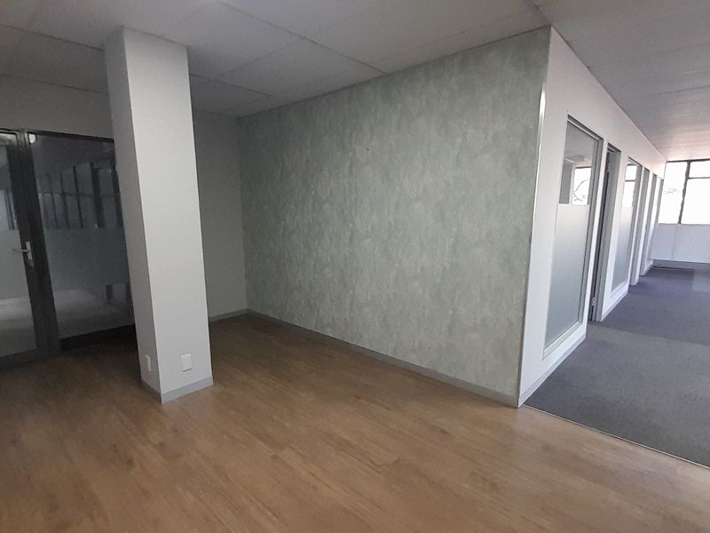 An empty, modern office space featuring a mix of laminate and carpet flooring, glass partitions, and a suspended ceiling.