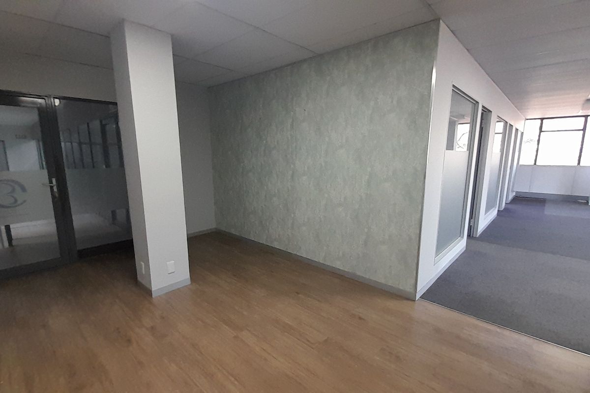 An empty, modern office space featuring a mix of laminate and carpet flooring, glass partitions, and a suspended ceiling.