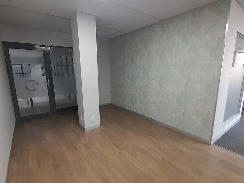 A vacant office space featuring laminate flooring, a structural column, and glass partition doors, offering a clean and professional environment.