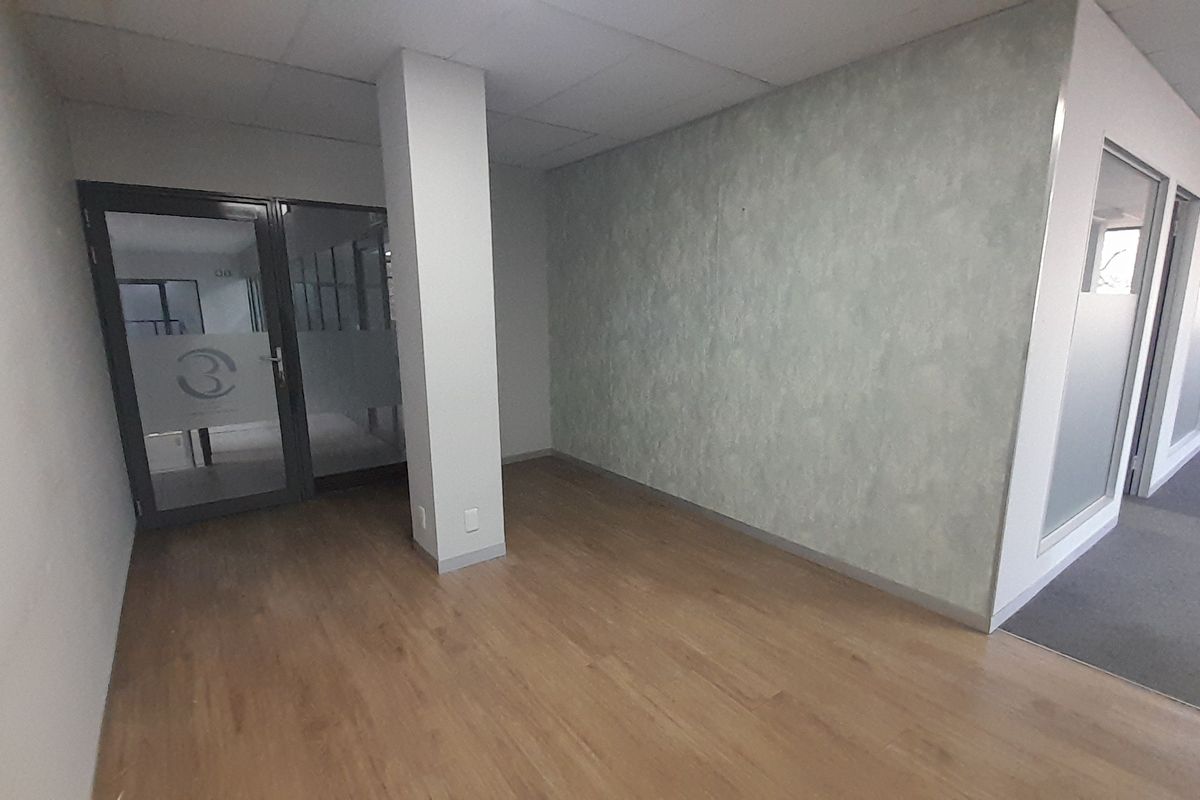 A vacant office space featuring laminate flooring, a structural column, and glass partition doors, offering a clean and professional environment.