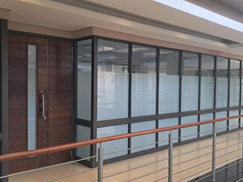 Modern office entrance featuring a solid timber door and extensive aluminium-framed glass partitioning with frosted privacy film, situated along a polished hallway.