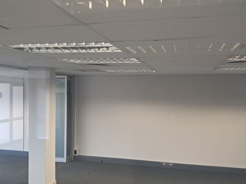 A clean, vacant office space featuring a suspended ceiling with recessed lighting, carpeted flooring, and a glass partition wall.