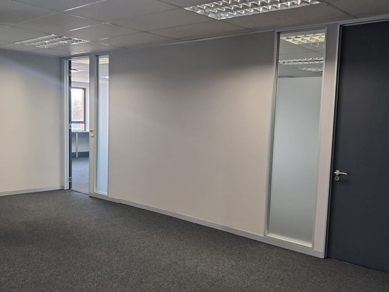 A clean, vacant office space featuring neutral carpet flooring, a suspended ceiling with recessed lighting, and a modern frosted glass partition.