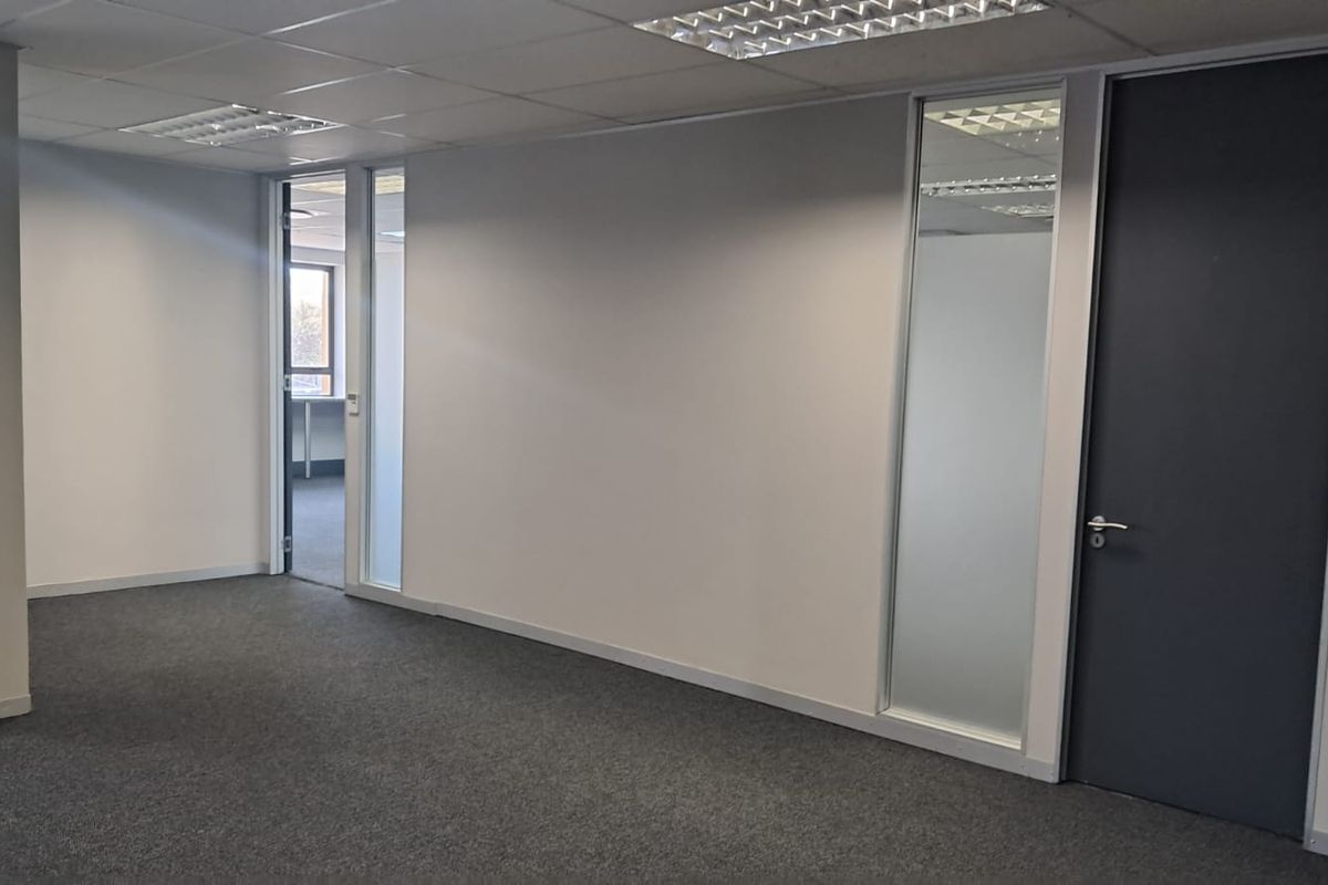 A clean, vacant office space featuring neutral carpet flooring, a suspended ceiling with recessed lighting, and a modern frosted glass partition.