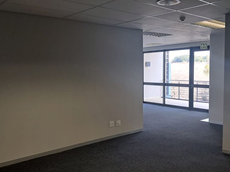 An open-plan office space featuring a suspended ceiling, carpeted flooring, and a glass door leading to an outdoor area.