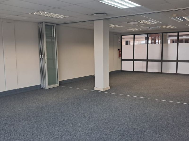 An open-plan office space featuring carpeted flooring, suspended ceilings with recessed lighting, and flexible folding glass partitions for versatile workspace configuration.