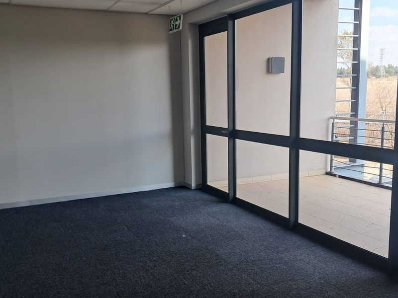 An empty office space featuring dark carpet flooring, a suspended ceiling, and large sliding glass doors providing access to an outdoor balcony.