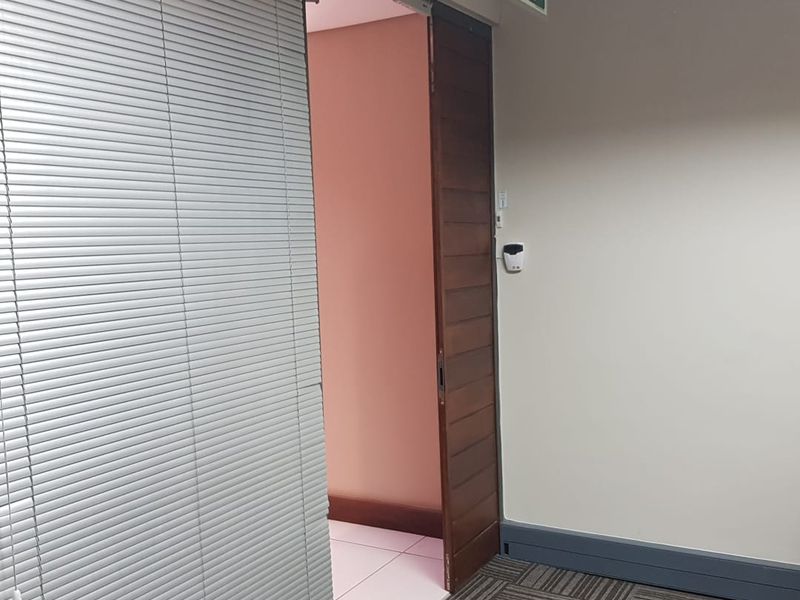 An office space featuring carpeted flooring, a sliding wooden door, and venetian blinds, providing a clean and functional professional environment.
