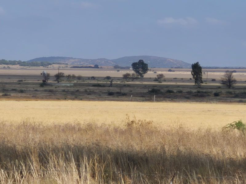 Expansive rural landscape view featuring open fields, distant hills, and a traditional farm windmill.