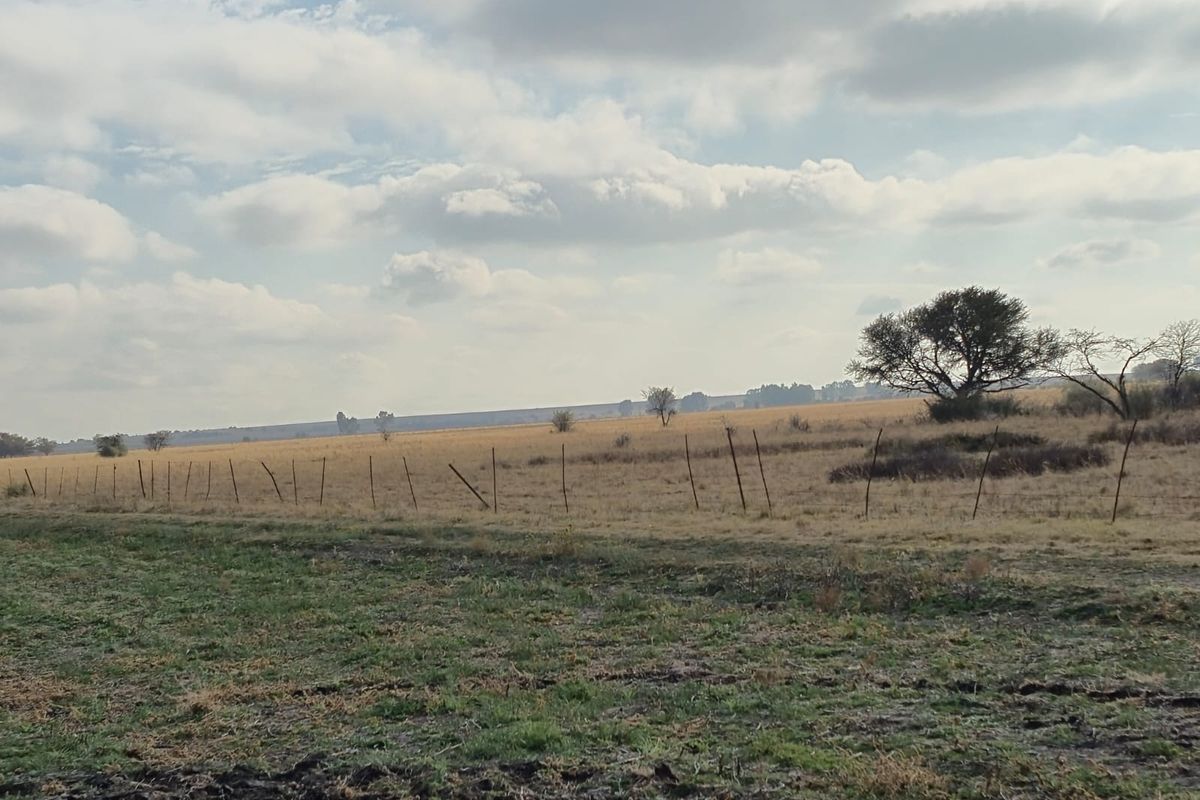 A wide-angle view of the expansive farm landscape featuring open fields and traditional wire boundary fencing.