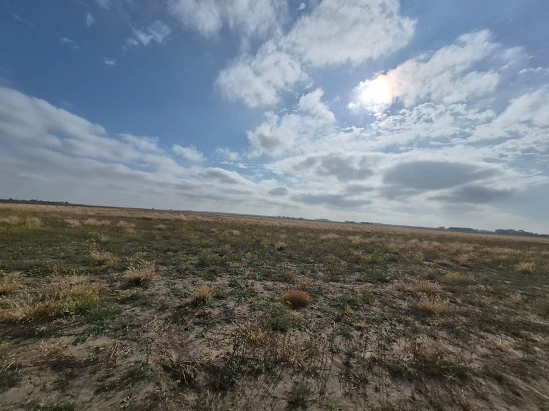 A wide-angle view of the expansive, open farmland landscape under a bright, cloudy sky.