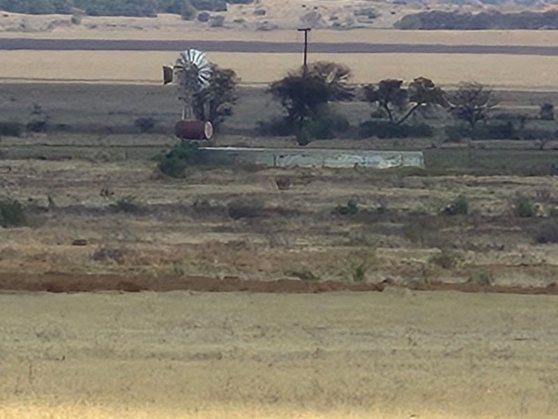 A distant view of the farm landscape featuring a traditional windmill and a water reservoir structure.