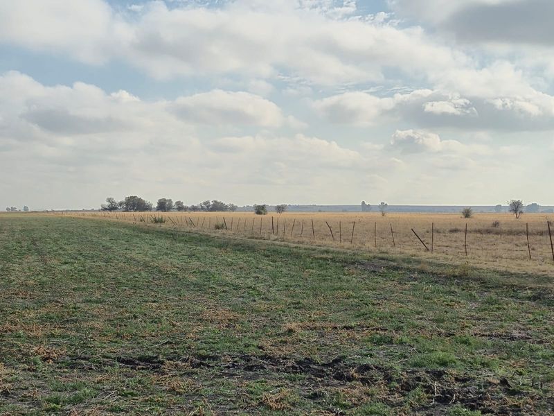 Expansive open farmland view featuring dry grass fields and traditional wire boundary fencing under a cloudy sky.