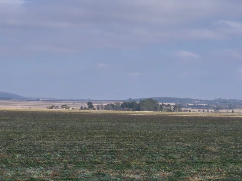 A wide-angle view of expansive open farmland and rural landscape under a cloudy sky.