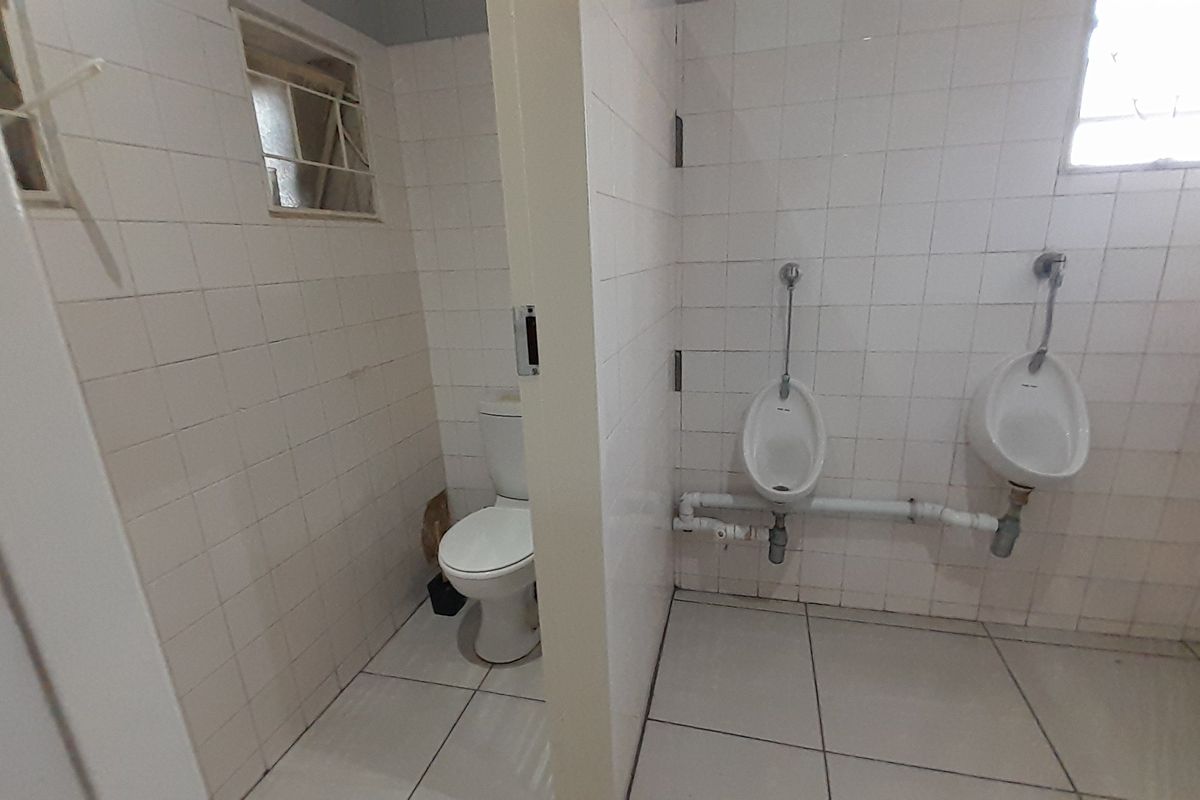 A functional office restroom featuring tiled walls and floors, equipped with a toilet and two wall-mounted urinals with exposed plumbing.