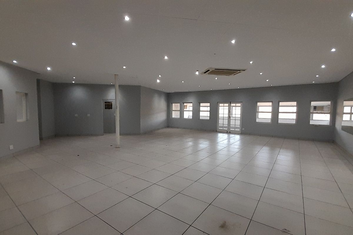 A spacious, open-plan office area featuring tiled flooring, recessed lighting, central air conditioning, and large windows providing ample natural light.