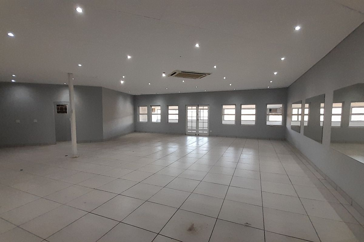 Spacious, open-plan office area featuring tiled flooring, recessed lighting, central air conditioning, and large wall-mounted mirrors, offering a versatile workspace.