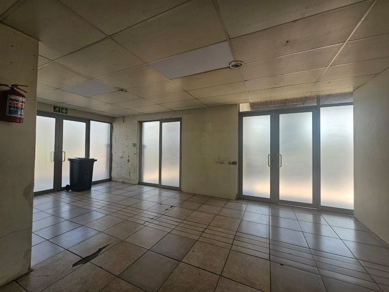 An empty open-plan retail space featuring tiled flooring, suspended ceilings, and multiple sliding glass doors providing natural light.
