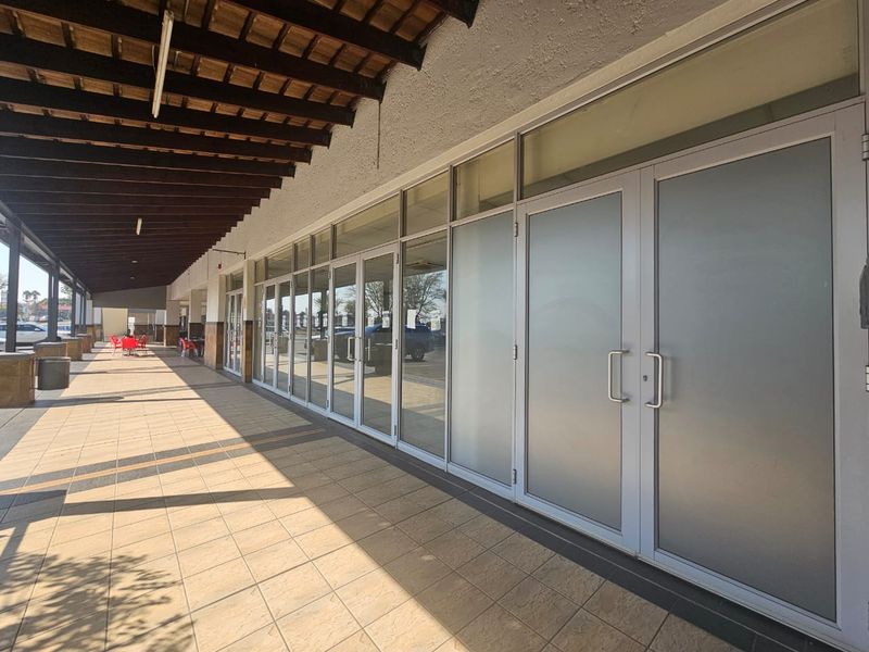 A retail storefront featuring a covered tiled walkway, timber pergola, and extensive aluminium-framed glass frontage with double entrance doors.