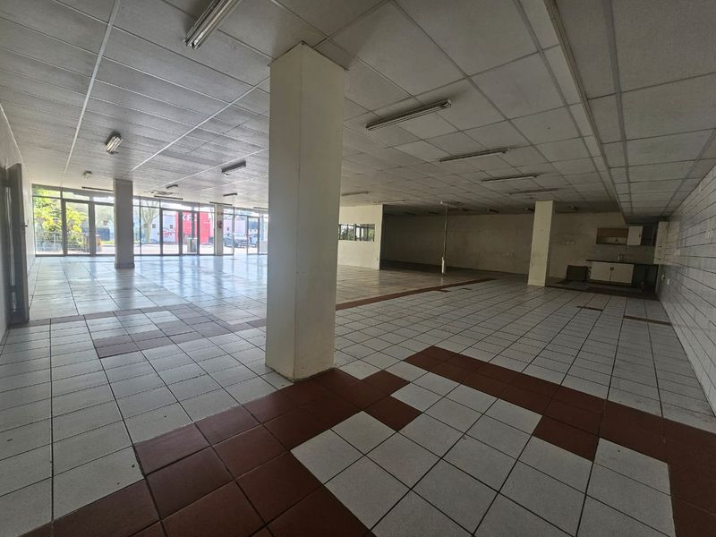 Spacious open-plan retail unit featuring large glass storefront, suspended ceilings, tiled flooring, and a small kitchenette area, suitable for various commercial business applications.