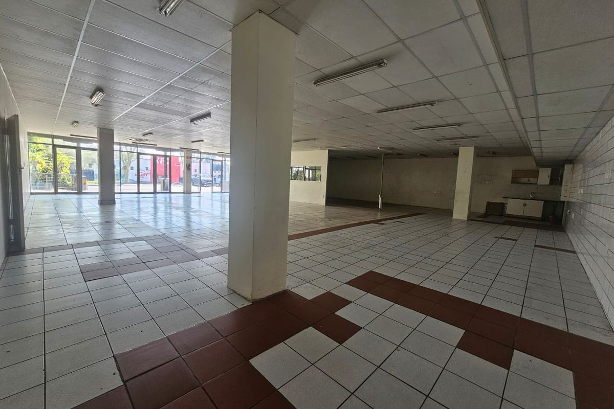 Spacious open-plan retail unit featuring large glass storefront, suspended ceilings, tiled flooring, and a small kitchenette area, suitable for various commercial business applications.