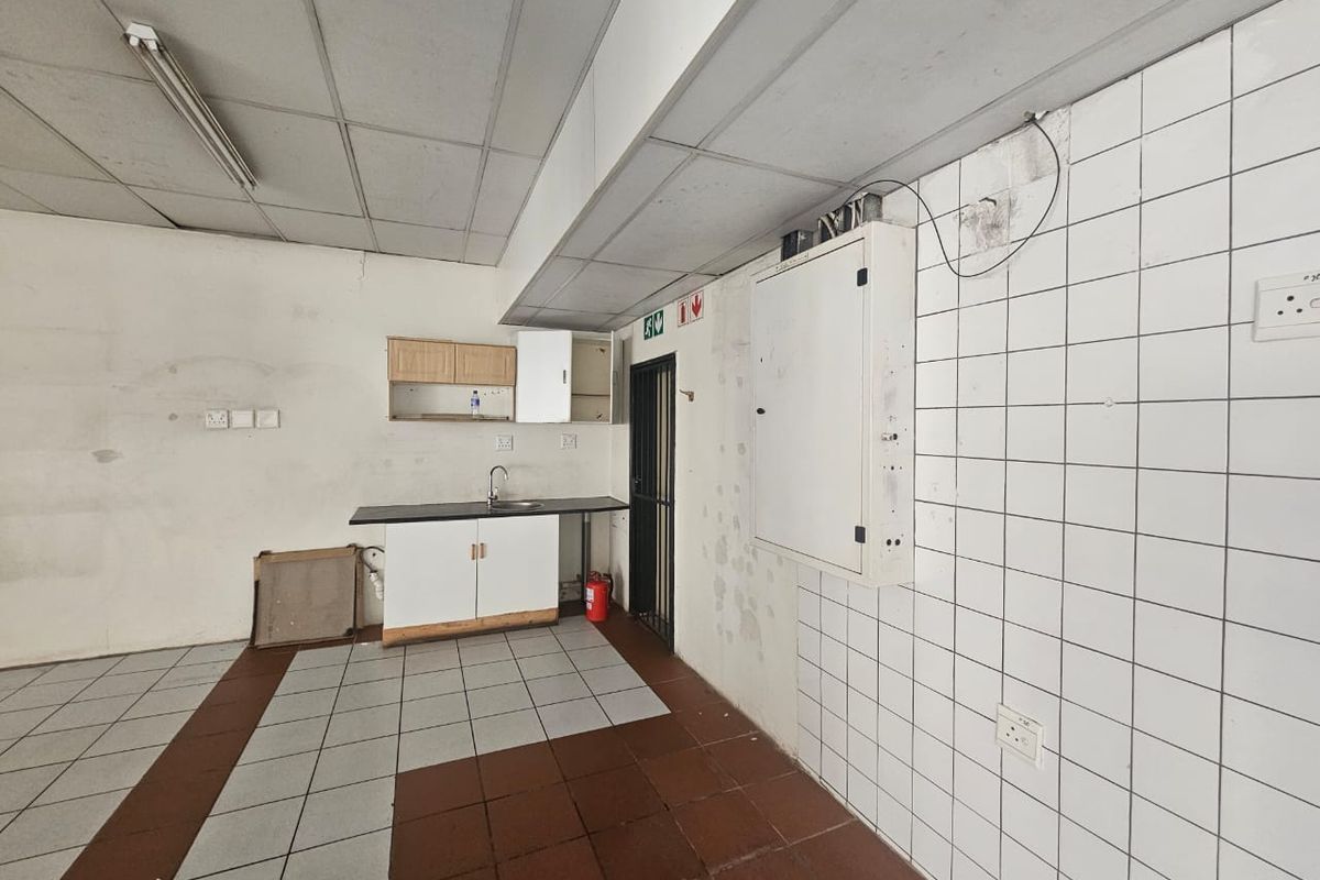 A basic kitchenette area featuring a sink, cabinetry, and tiled flooring, currently in need of cosmetic refurbishment and wall repairs.
