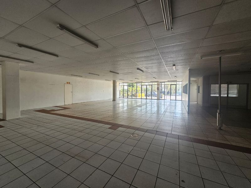 A spacious, vacant open-plan retail unit featuring ceramic tiled flooring, a suspended ceiling with integrated lighting, and large glass storefront windows.