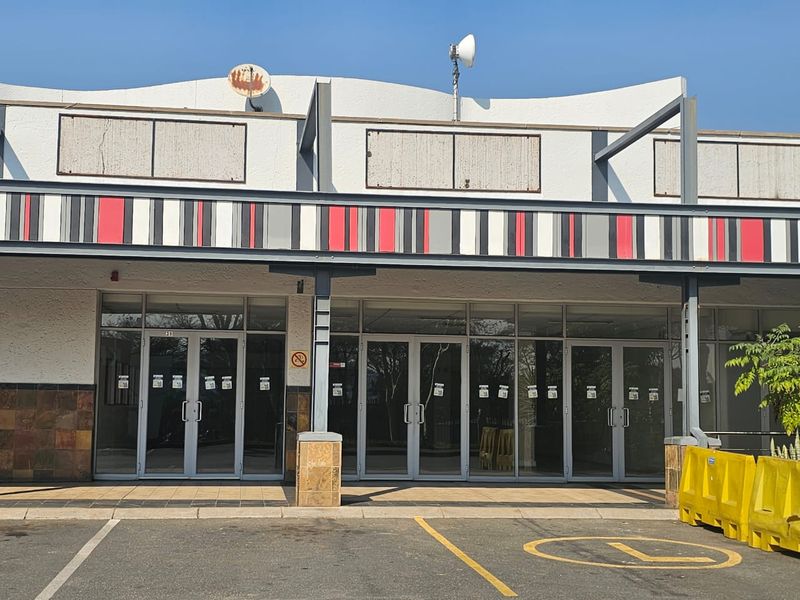 Front elevation of a retail unit featuring glass storefront doors, a covered walkway with a metal awning, and tiled base detailing.