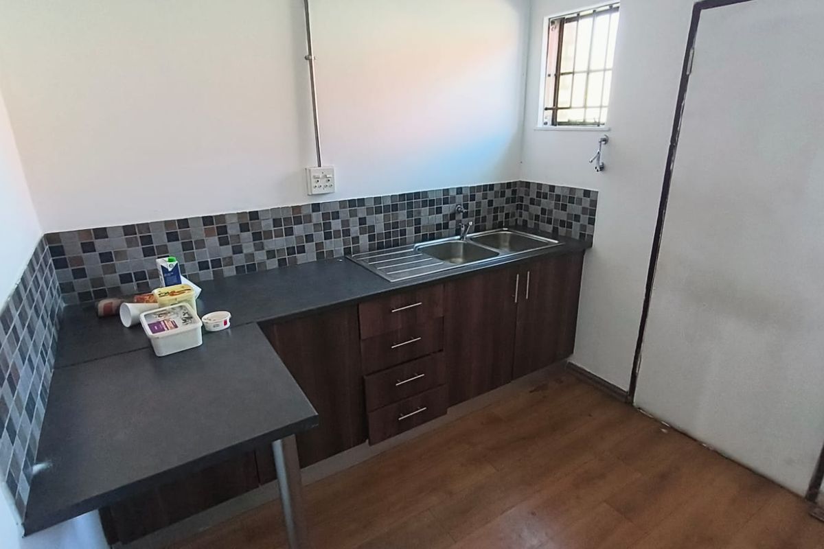 A compact kitchen area featuring dark wood cabinetry, laminate countertops, a double stainless steel sink, and a mosaic tile backsplash.