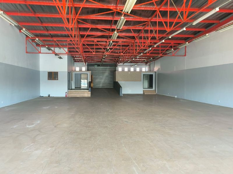 Spacious open-plan industrial warehouse featuring high exposed steel roof trusses, concrete flooring, and a large roller shutter door for easy access.