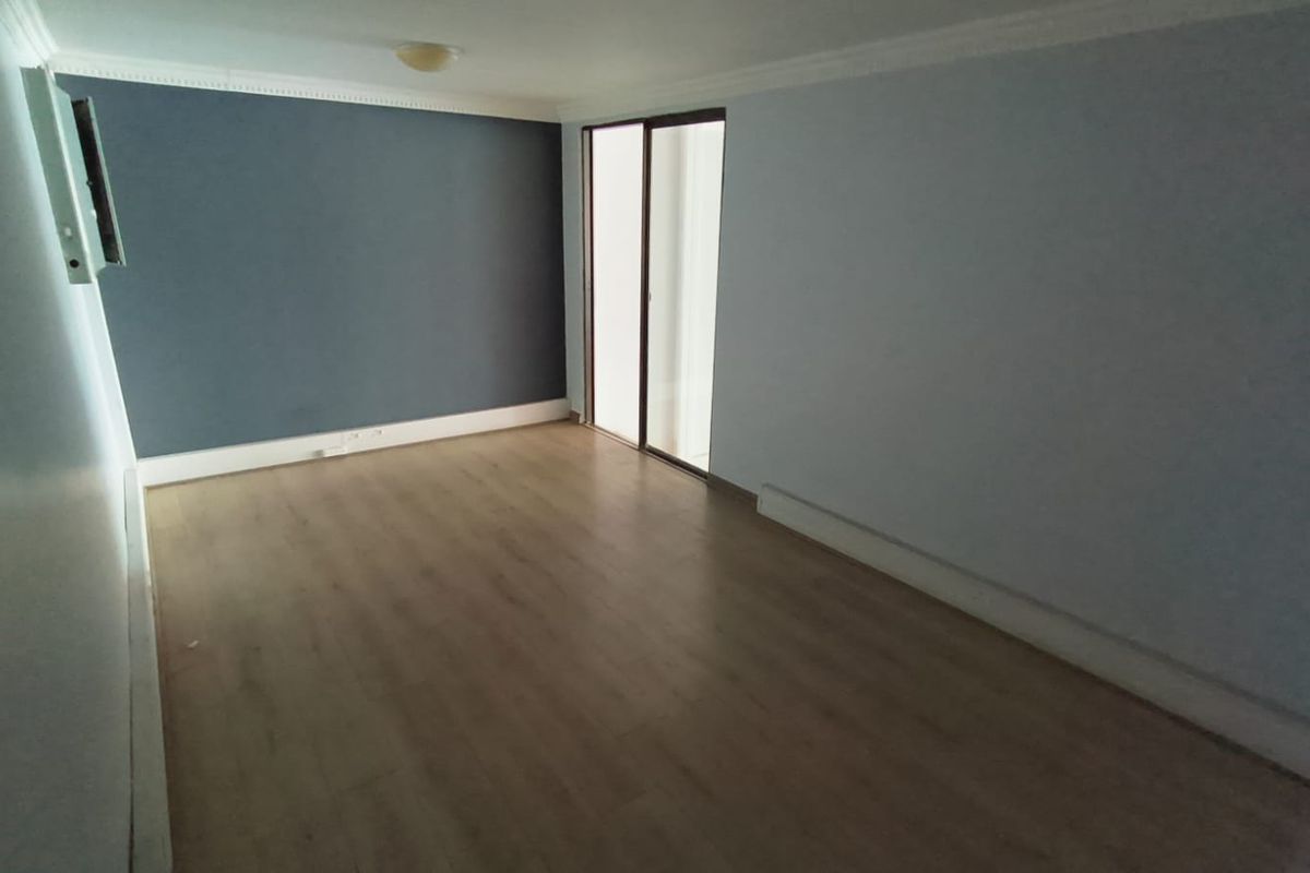 An empty living room featuring laminate flooring, a dark accent wall, crown molding, and a sliding glass door providing natural light.