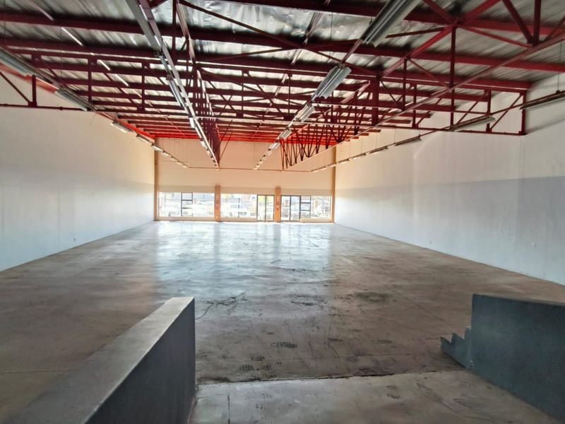Spacious open-plan retail unit featuring high exposed steel roof trusses, polished concrete flooring, and large glass windows providing ample natural light.