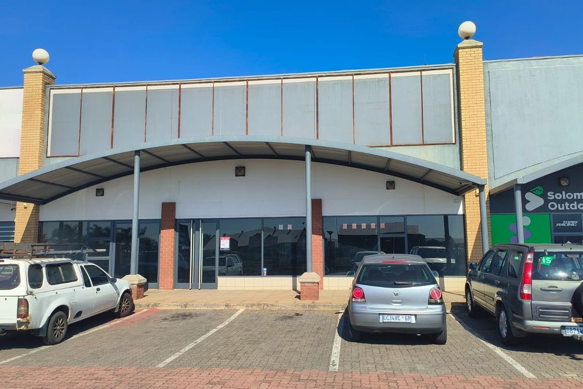 Front elevation of a retail unit featuring a curved metal awning, glass storefront, and dedicated paved parking space.